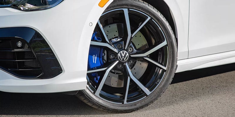 Close-up of a white car's front wheel, showcasing the black alloy rim with silver accents and blue brake calipers.