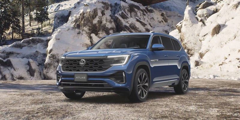 Blue 2024 Volkswagen Atlas SUV parked on a dirt road in a snowy, mountainous landscape.