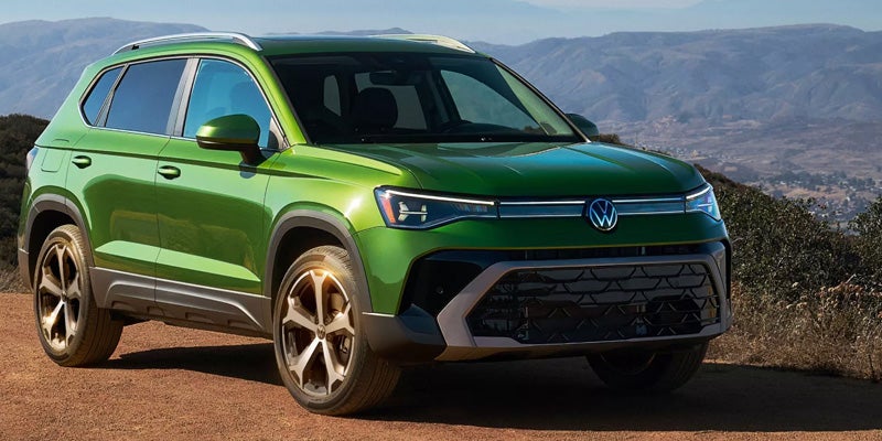 A bright green compact SUV, viewed from the front quarter, on a dirt path with mountains in the background.