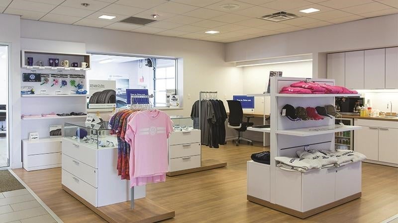 A bright, modern dealership showroom with branded apparel and accessories displayed on white shelves and racks.